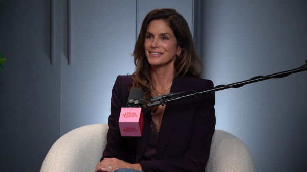 Cindy Crawford wearing a blazer and sitting behind a microphone